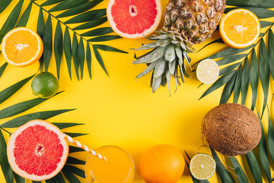 Summer fruits. Tropical palm leaves, pineapple, coconut, grapefruit, orange and glass of juice on yellow background. Flat lay, top view, copy space