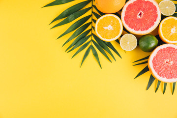 Summer fruits. Tropical palm leaves, lime, grapefruit and orange on yellow background. Flat lay, top view, copy space