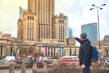 Young male tourist walking around the city and watching on Palace of Culture and Science in Warsaw. Having a happy vacation in Poland