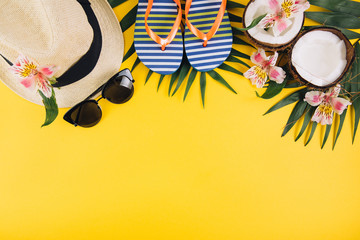 Tropical palm leaves, hat, slippers, sunglasses, coconut on yellow background. Summer concept. Flat lay, top view, copy space