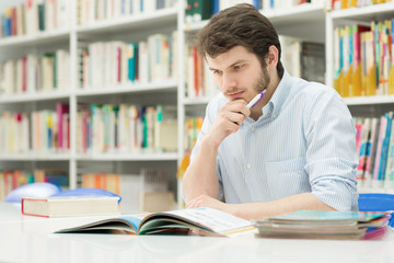 Handsome young male student doing homework at the library