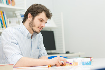 Obraz premium Handsome young male student doing homework at the library
