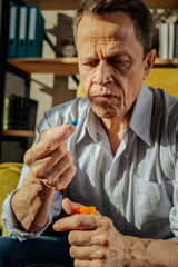 Focused old upset man holding an orange container with pills