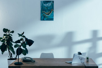Laptop with webcam, lamp and telephone on table in office