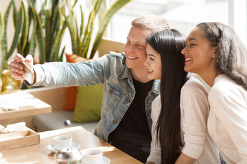 Young cheerful friends using smart phone together at the coffee shop