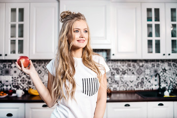 Blonde woman wearing pajama standing with apple and enjoing the morning