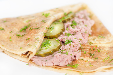 Thin delicious pancake with meat pate and cucumber on white