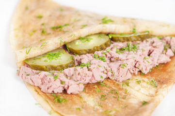 Thin delicious pancake with meat pate and cucumber on white