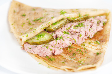 Thin delicious pancake with meat pate and cucumber on white