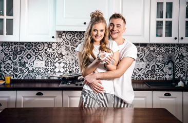 Smiling young man embracing woman from behind in the kitchen at home