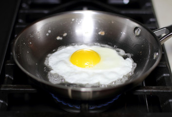 Egg sunny side up frying in a pan on the stove.