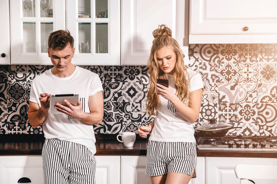 Internet addicted couple standing at tge kitchen with the gadgets