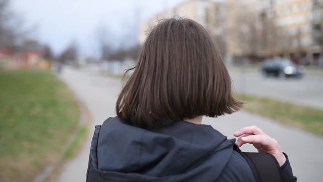 Rear view of woman pulling down backpack on street, slow motion handheld footage