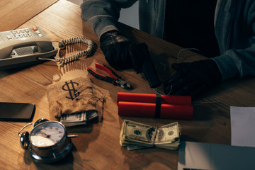 Cropped view of criminal in black gloves with gun, dynamite and dollar banknotes