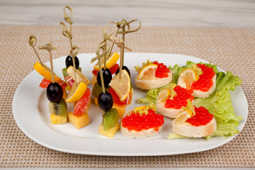 Appetizer with lemon and olives and sandwiches with red caviar on an oval white dish.