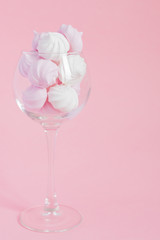 Obraz na płótnie Canvas White and pink twisted meringues in a vine glass on pink background. French dessert prepared from whipped with sugar and baked egg whites. Greeting card with copy space