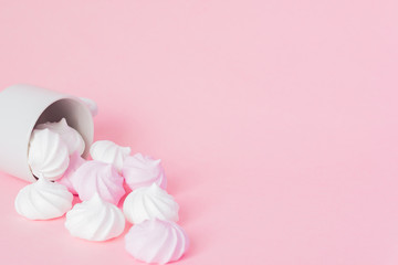 Obraz na płótnie Canvas White and pink twisted meringues in a small porcelain coffe cup on pink background. French dessert prepared from whipped with sugar and baked egg whites. Greeting card with copy space