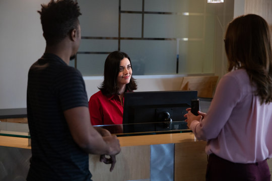 Friendly Receptionist Greeting Two People In Business Lobby