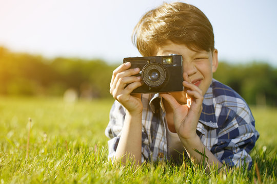 Little boy resting at the park taking pictures with a retro camera