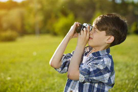 Little boy resting at the park taking pictures with a retro camera