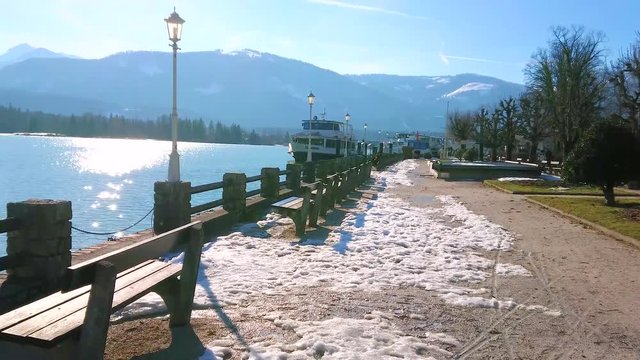 ST WOLFGANG, AUSTRIA - FEBRUARY 23, 2019: Relax in small park on embankment of Wolfgangsee lake with small benches, old-styled streetlights and ferry port on background, on February 23 in St Wolfgang.