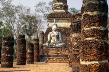 Fototapeta premium Ancient statue of a meditating Buddha among columns in Sukhothai National Park, Thailand