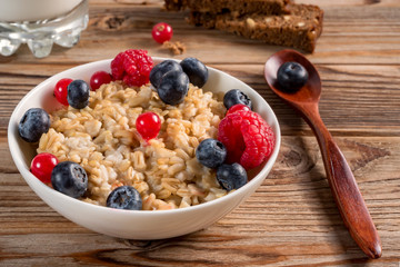 Close up view of porridge with blueberries and raspberries and grain bread on wooden background. Soft focus.