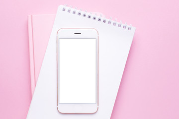 Mobile phone mock up and notebook on pink pastel table top view in flat lay style. Woman working desk.