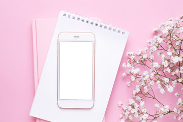 Mobile phone mock up and white flowers on pink pastel table top view in flat lay style. Woman working desk.