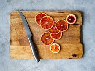 Fresh red blood oranges with slices on a vintage old cutting wooden board on a gray background with metal knife. Top View, selective focus.