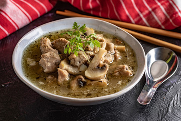 Soup with pieces of pork and mushrooms in bowl.