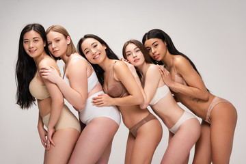 five happy young multiethnic women in underwear leaning on each other isolated on grey, body positivity concept