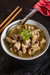 Soup with pieces of pork and mushrooms in bowl.