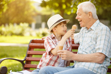 Little boy and his grandfather eating ice cream together at the park