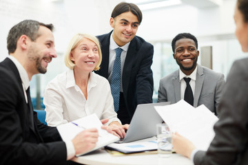 Group of smiling businesspeople discussing work during meeting with mature businesswoman heading table, copy space