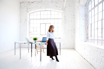 Attractive young creative woman standing at office desk and looking thoughtfully