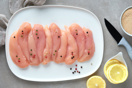 Raw chicken fillet. Meat with breadcrumbs, herbs , lemon and cooking oil. Top view on light background.