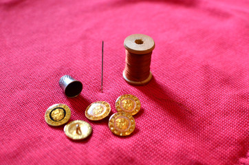 Accessories for sewing and darning clothes: needle, thread and thimble on a red background of wool...