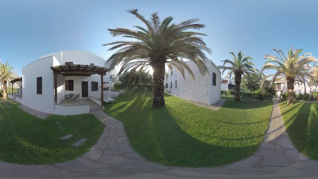 360 VR Video. Villas for rent among the olive trees and big palms. Sprinkler system watering green lawns. Cottages for great holidays at Trikorfo Beach resort, Greece