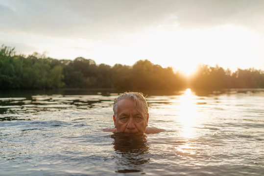 Senior man swimming in a lake at sunset
