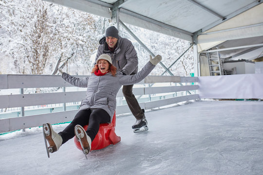 Couple ice skating, using seal sledge to push woman