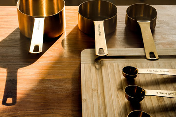 Golden kitchen pots and scoops arranged in a line on a wooden chopping board and table. Kitchen...