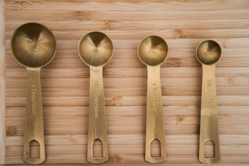 Golden kitchen scoops arranged in a line on a wooden chopping board. Kitchen scoops have capacity...