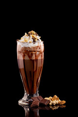 Closeup glass of chocolate milk shake with nuts decorated with whipped cream isolated at black background.