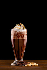 Closeup glass of chocolate milk shake with nuts decorated with whipped cream isolated at wooden board background.