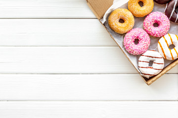 Glazed decorated donuts in box on white wooden background flat lay mock up