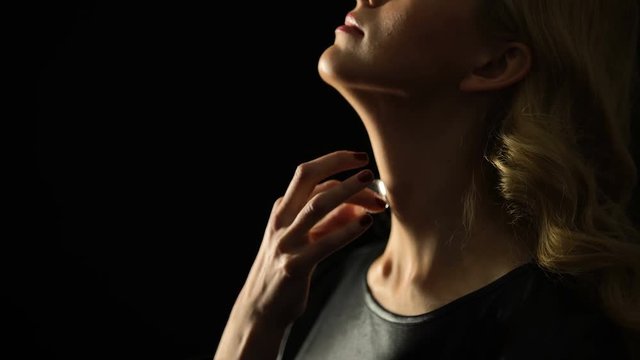 Confident blond woman stroking neck with ice cube against black background