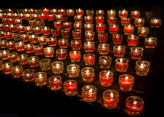 Opferlichter brennen in der Kirche - viele rote Kerzen auf schwarzem Hintergrund
