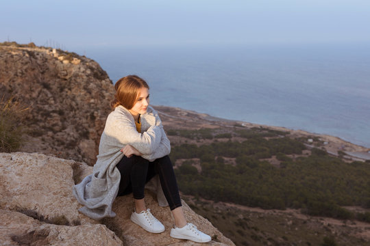 Spain, Alicante, Santa Pola, Cape Santa Pola, young woman sitting on rock at sunset
