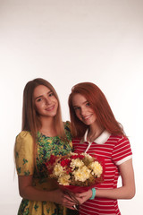 The portrait of two young smiling lades redhead and brunette with a bouquet in there hands isolated over white background posing